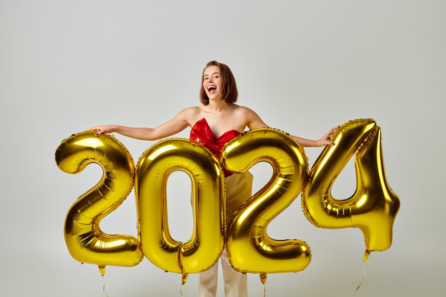 A photo of a woman holding golden balloons that spell out 2024